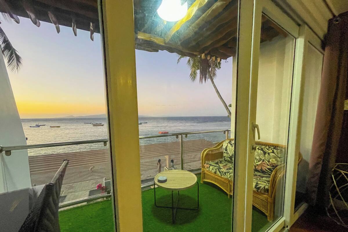 Un balcón con vista a la playa, una pequeña mesa redonda y un sofá de mimbre.