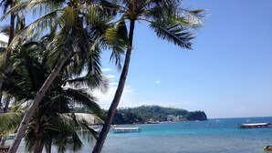 A beach with palm trees, clear blue water, and boats. - Montani Beach Resort Puerto Galera powered by Cocotel (Puerto Galera)