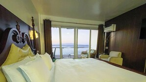 A hotel room with a large bed, a chair, a small table, and a view of the sea. - Montani Beach Resort Puerto Galera powered by Cocotel (Puerto Galera)