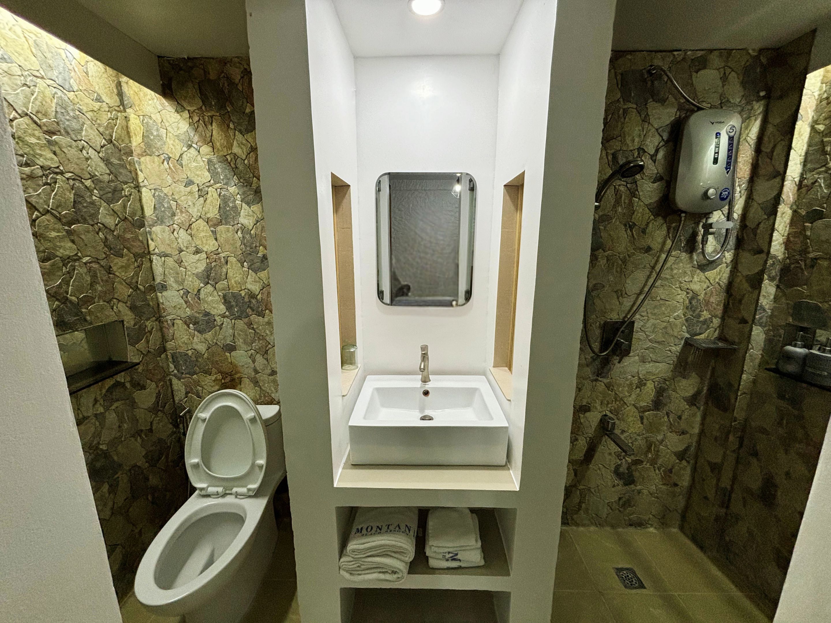 A bathroom with a stone wall, a white sink, a toilet, and a shower area.