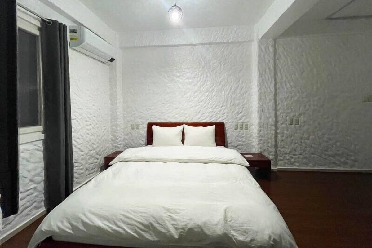 Un dormitorio con cama, ventana con cortinas y pared con textura.