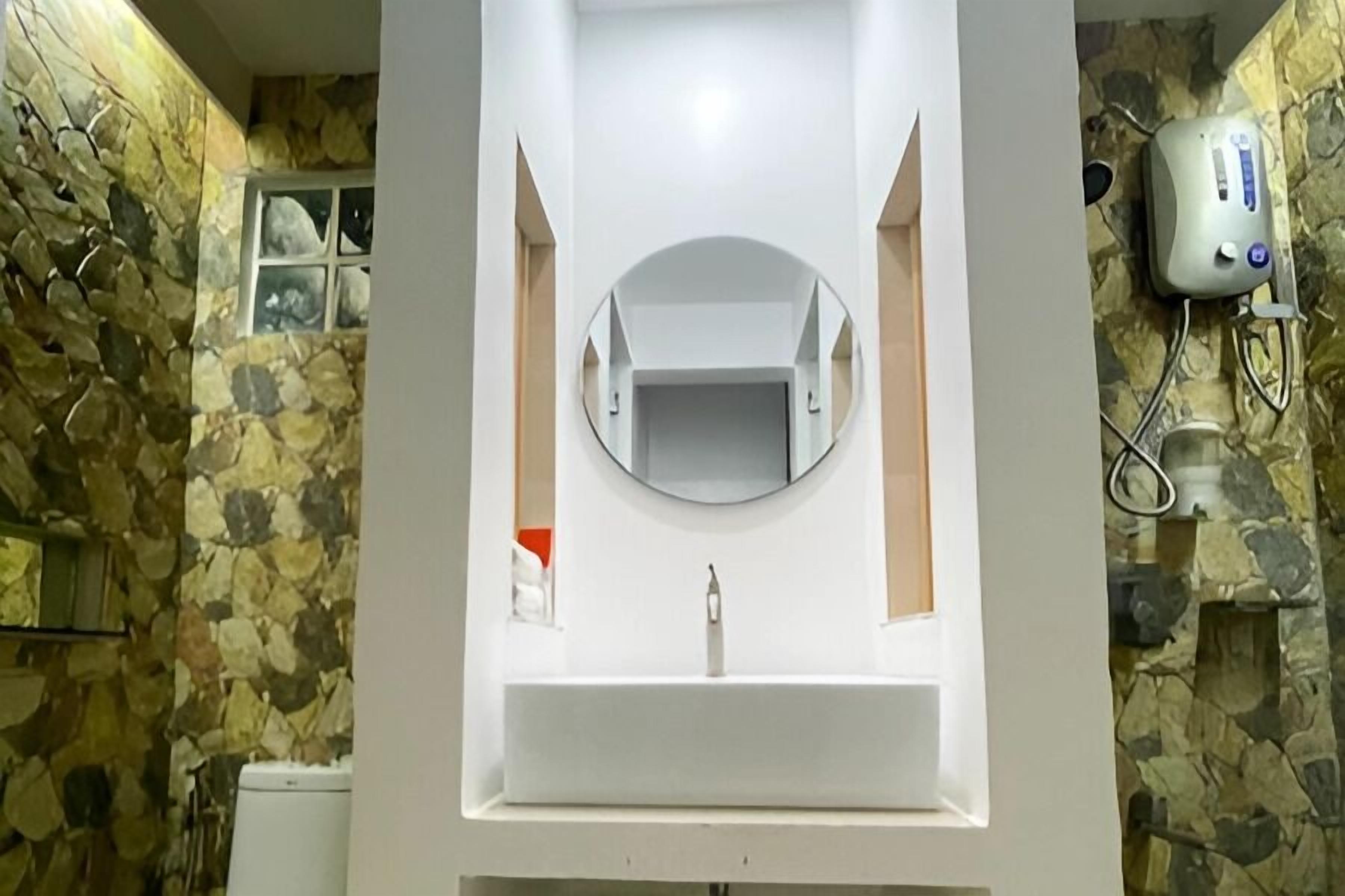A bathroom with a stone wall, a white sink, and a mirror.