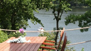 A wooden table with chairs and a rope barrier overlooking a lake with a boat. - Ferienwohnpark Silbersee (Frielendorf)