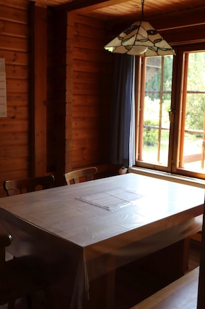 Ein Holzblockhaus-Interieur mit einem großen Esstisch, Stühlen und einer Hängelampe.