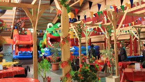 An indoor venue with wooden structures, inflatable play areas, and tables with red tablecloths. - Ferienwohnpark Silbersee (Frielendorf)