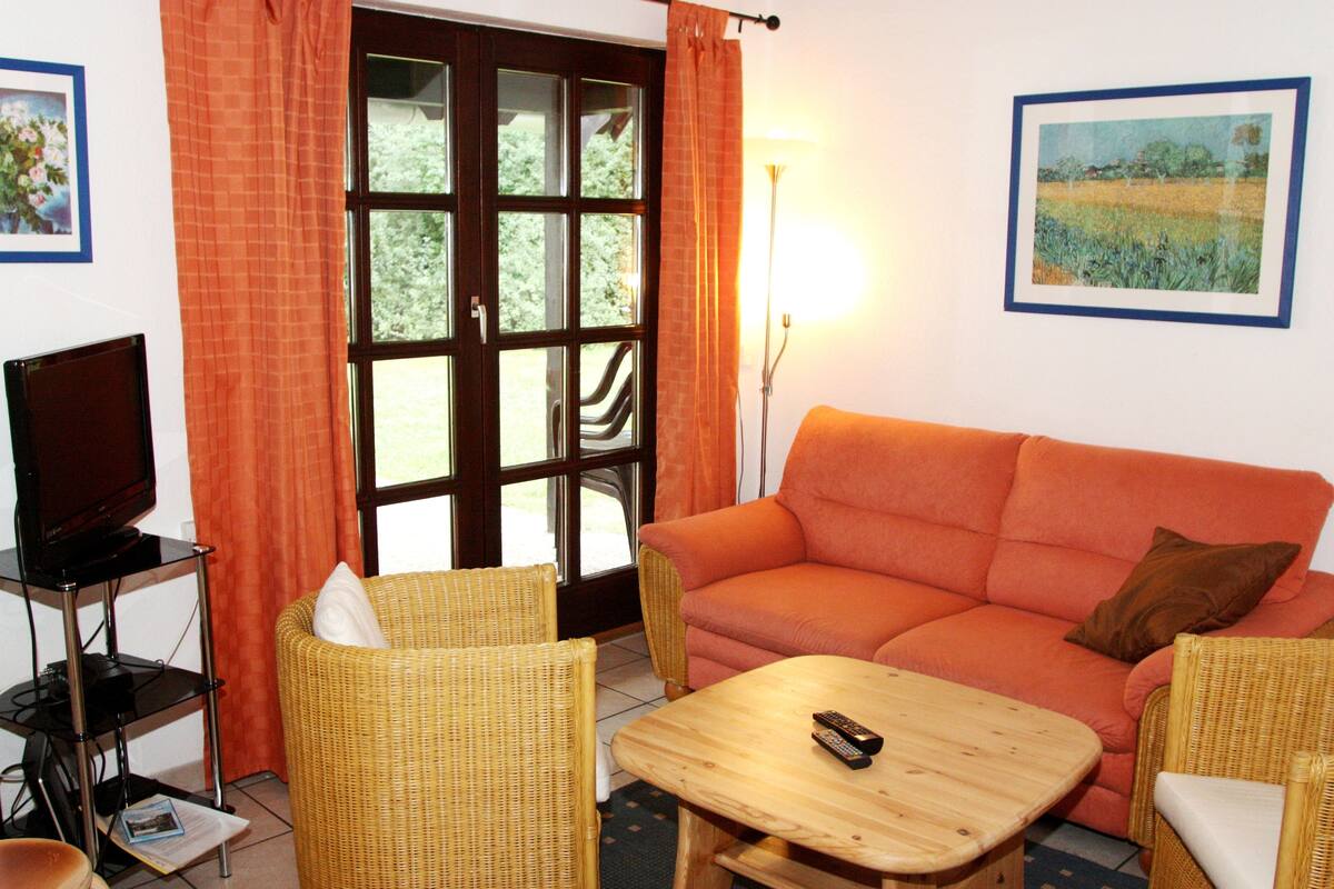 A living room with a sofa, two wicker chairs, a wooden coffee table, a television on a stand, and a large window with curtains.