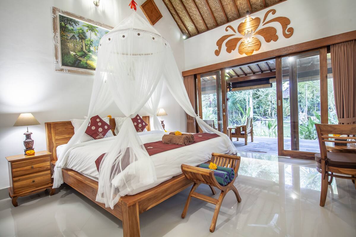 A spacious bedroom with a wooden bed, a canopy, and a view of the garden through large sliding doors.