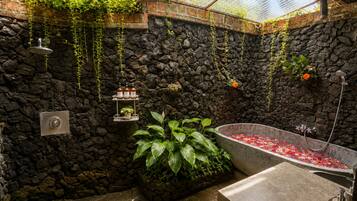 A bathroom with a stone wall, a large bathtub, and a shower.
