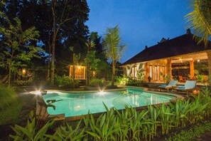 A swimming pool with lounge chairs and a covered seating area surrounded by tropical vegetation. - Jero Sebali Villa (Ubud)