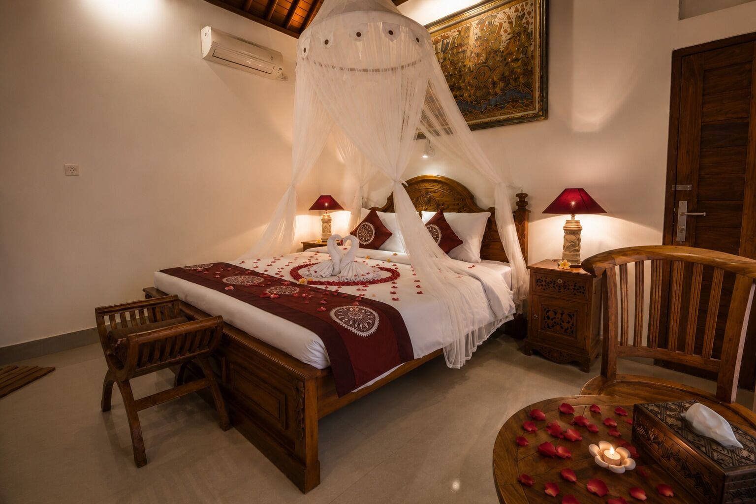 A bed with a canopy, two bedside lamps, a wooden chair, a bedside table with a candle, and a decorative wall piece.