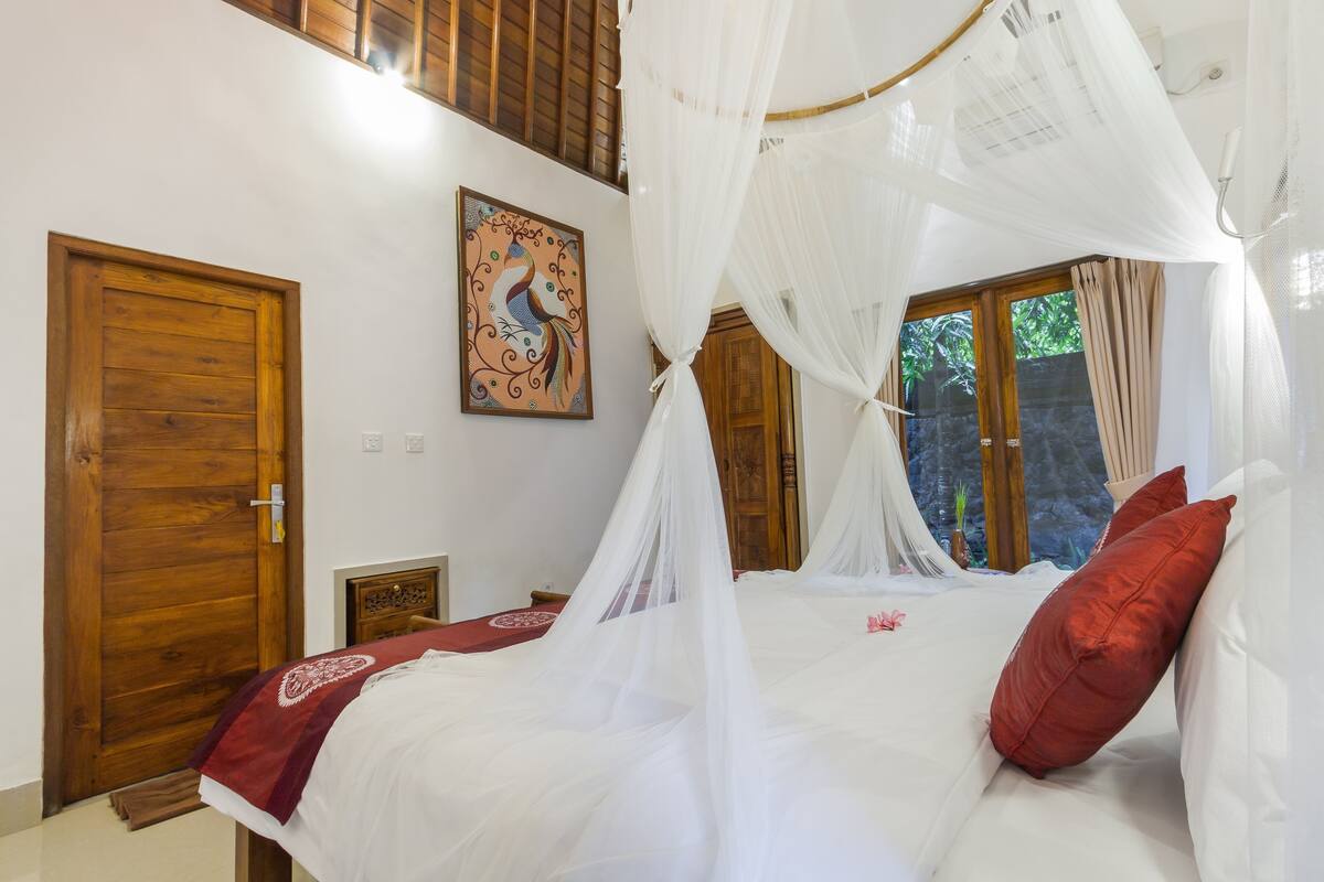 A bedroom with a bed under a canopy, a wooden door, and a wall-mounted picture.