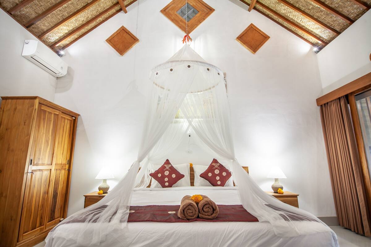 A bedroom with a canopy bed, wooden wardrobe, and a ceiling with exposed beams.