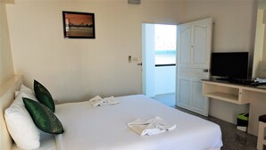 A hotel room with a bed, pillows, a TV, and a door leading to a balcony. - Chouaprom Mansion (Nakhon Si Thammarat)