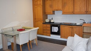 A compact kitchen with wooden cabinets, a glass dining table, and a built-in oven. - Apartment Northfields (London)