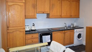 Una cocina con armarios de madera, encimera negra, lavadora y mesa de vidrio.