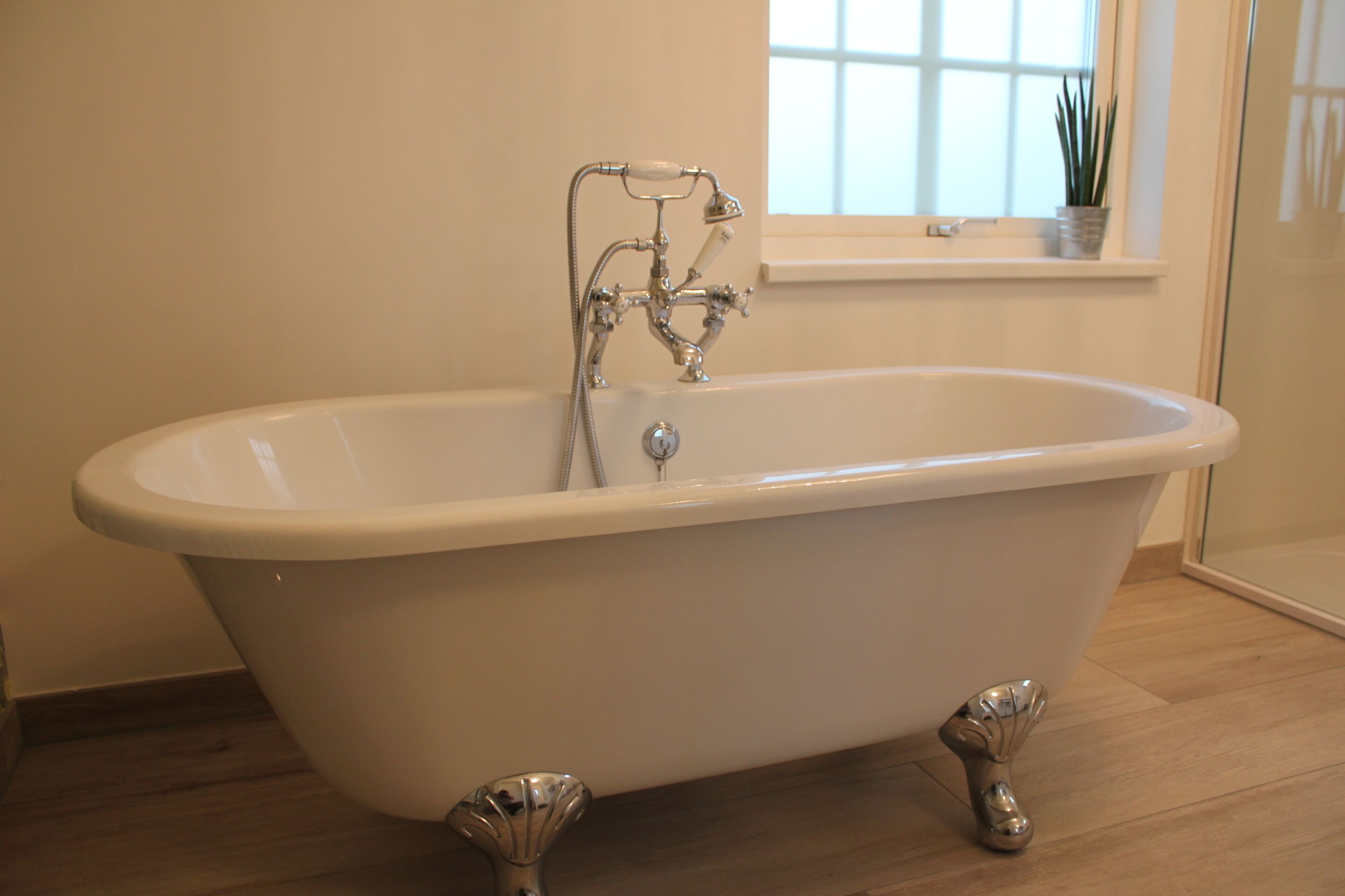 Une baignoire sur pieds avec un intérieur blanc, une fenêtre au-dessus et une plante posée sur le rebord de la fenêtre.