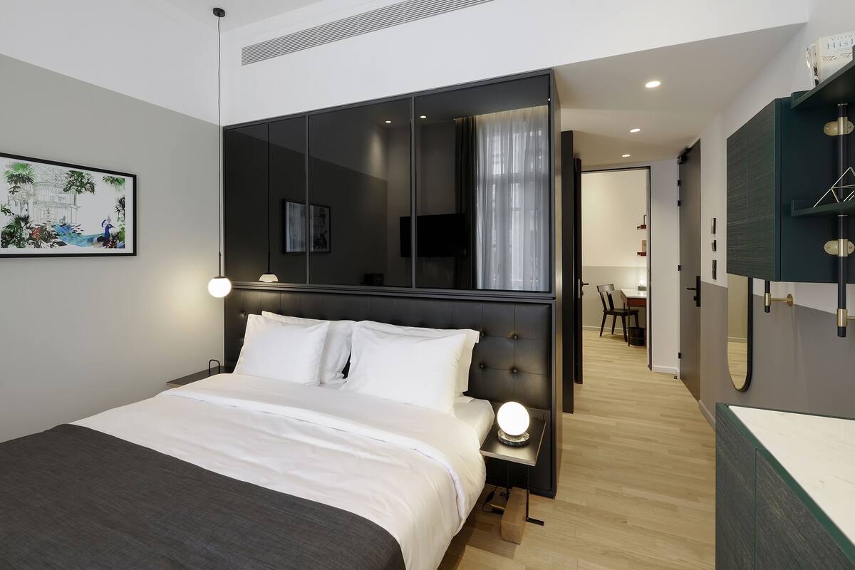 Ein modernes Schlafzimmer mit einem großen Bett, Nachttischlampen, einem Spiegel und Blick in den angrenzenden Essbereich.