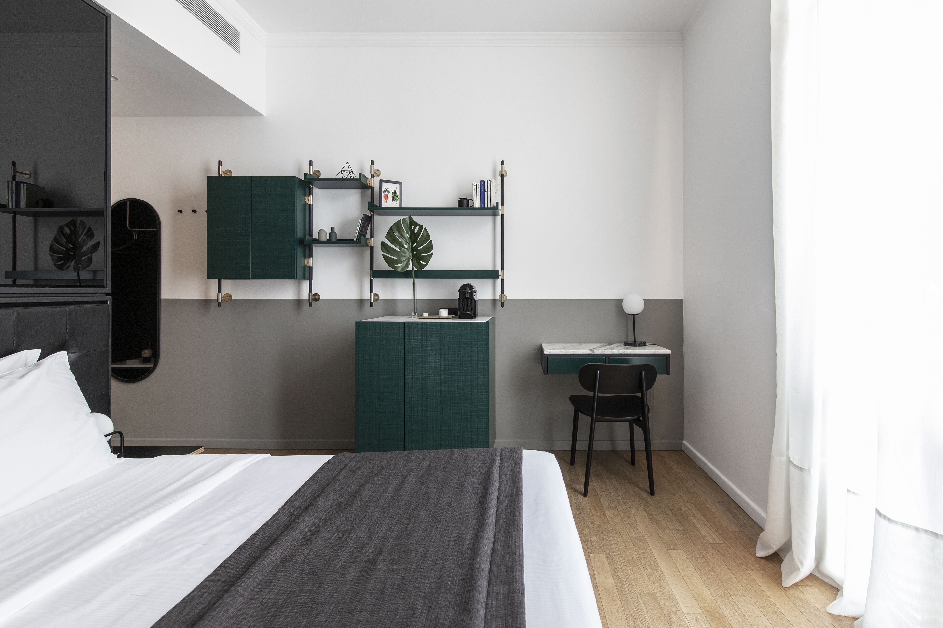 A modern bedroom with a bed, a desk, and a chair. There are shelves with decorative items and a mirror.