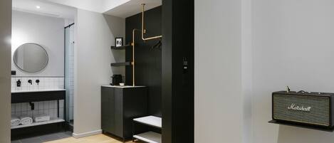 A modern bathroom with a black and white color scheme, a round mirror, a coffee machine, and a shelf with toiletries.