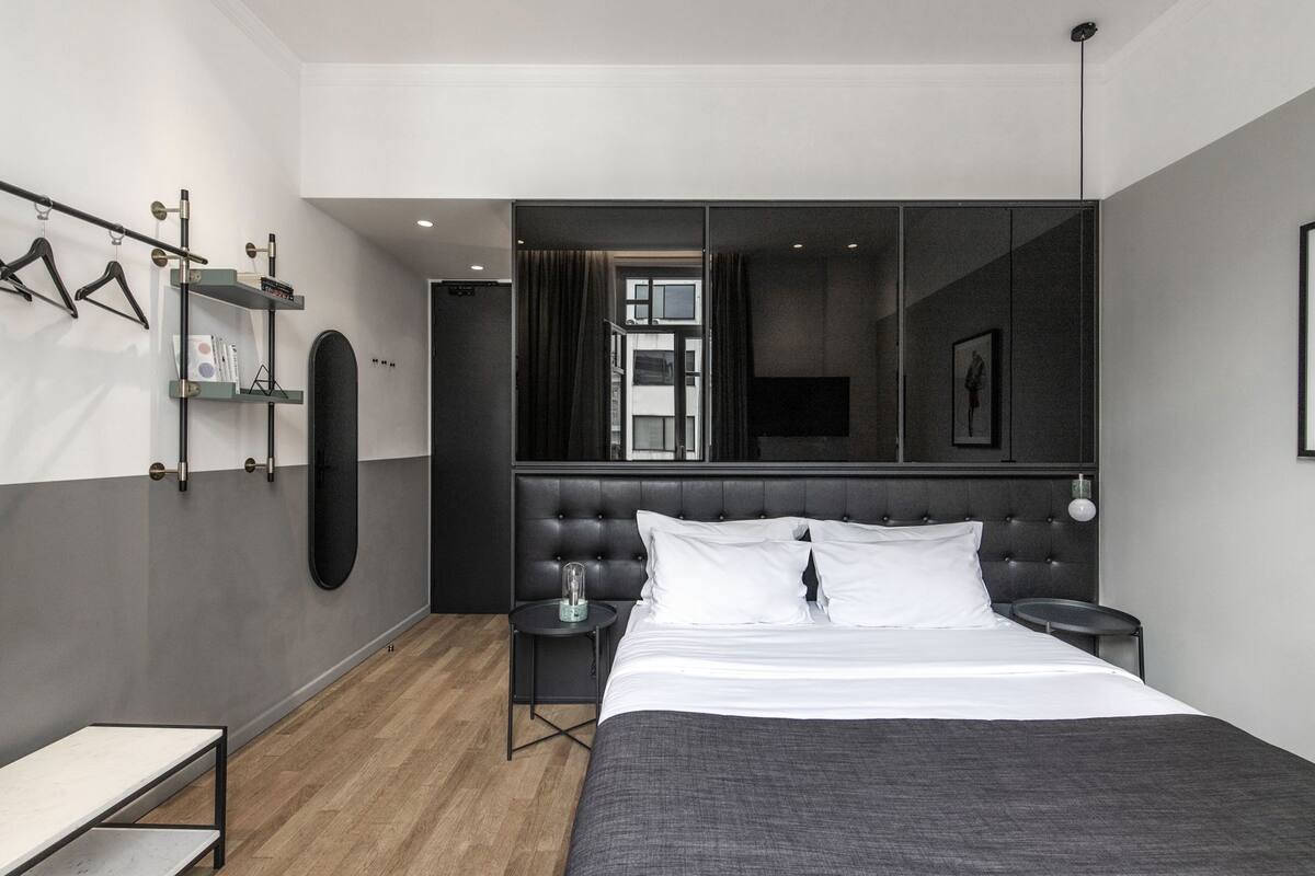 Ein modernes Hotelzimmer mit einem großen Bett, einem Nachttisch, einem kleinen Beistelltisch, einem Spiegel und einem Kleiderschrank.