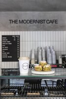 Una cafetería llamada "The Modernist Cafe" con un menú, una taza de café y pasteles a la vista.