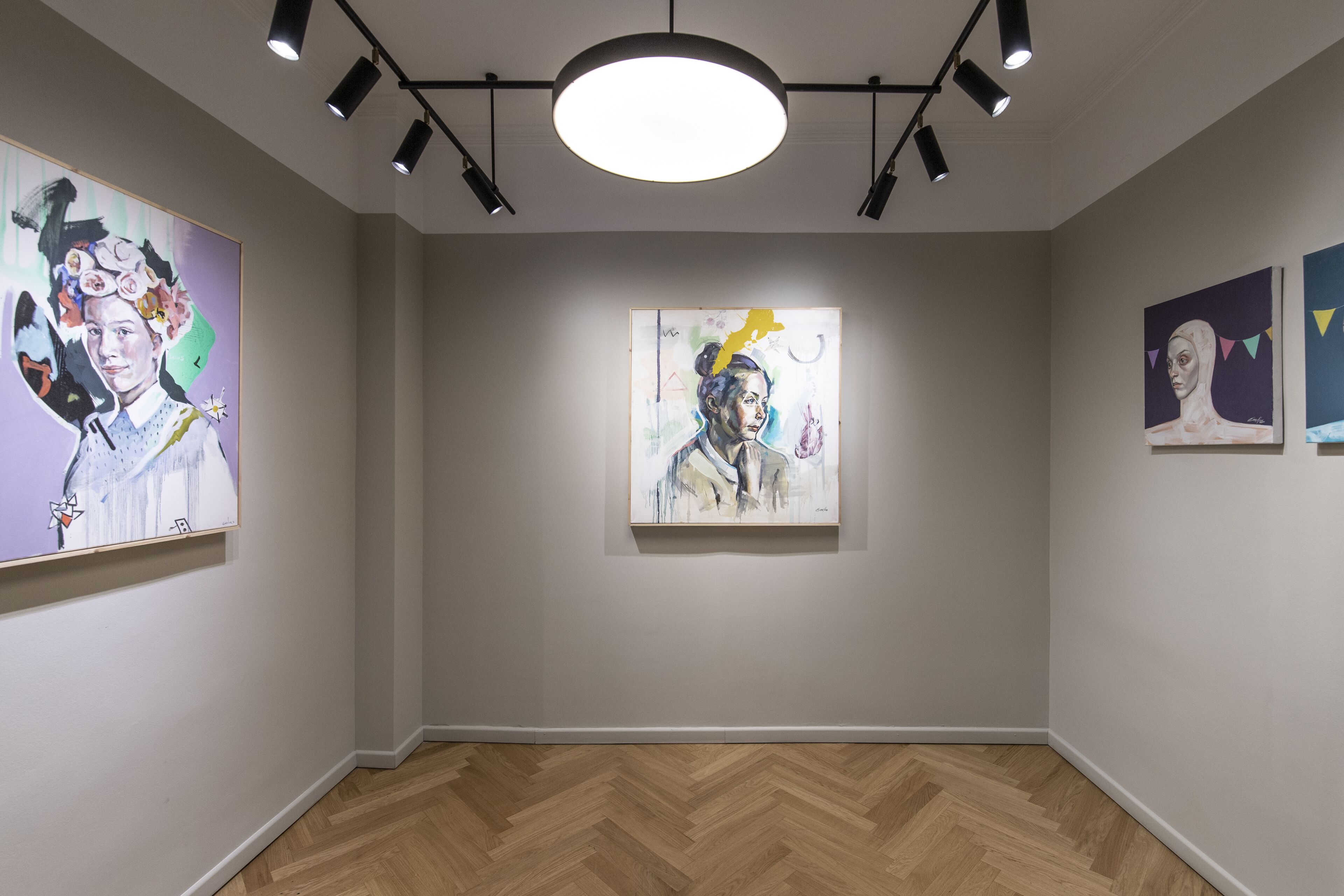 An art gallery with three paintings on the walls and a wooden herringbone floor.