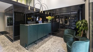 Un área de recepción moderna con un mostrador verde, sillas negras y una planta grande en maceta.