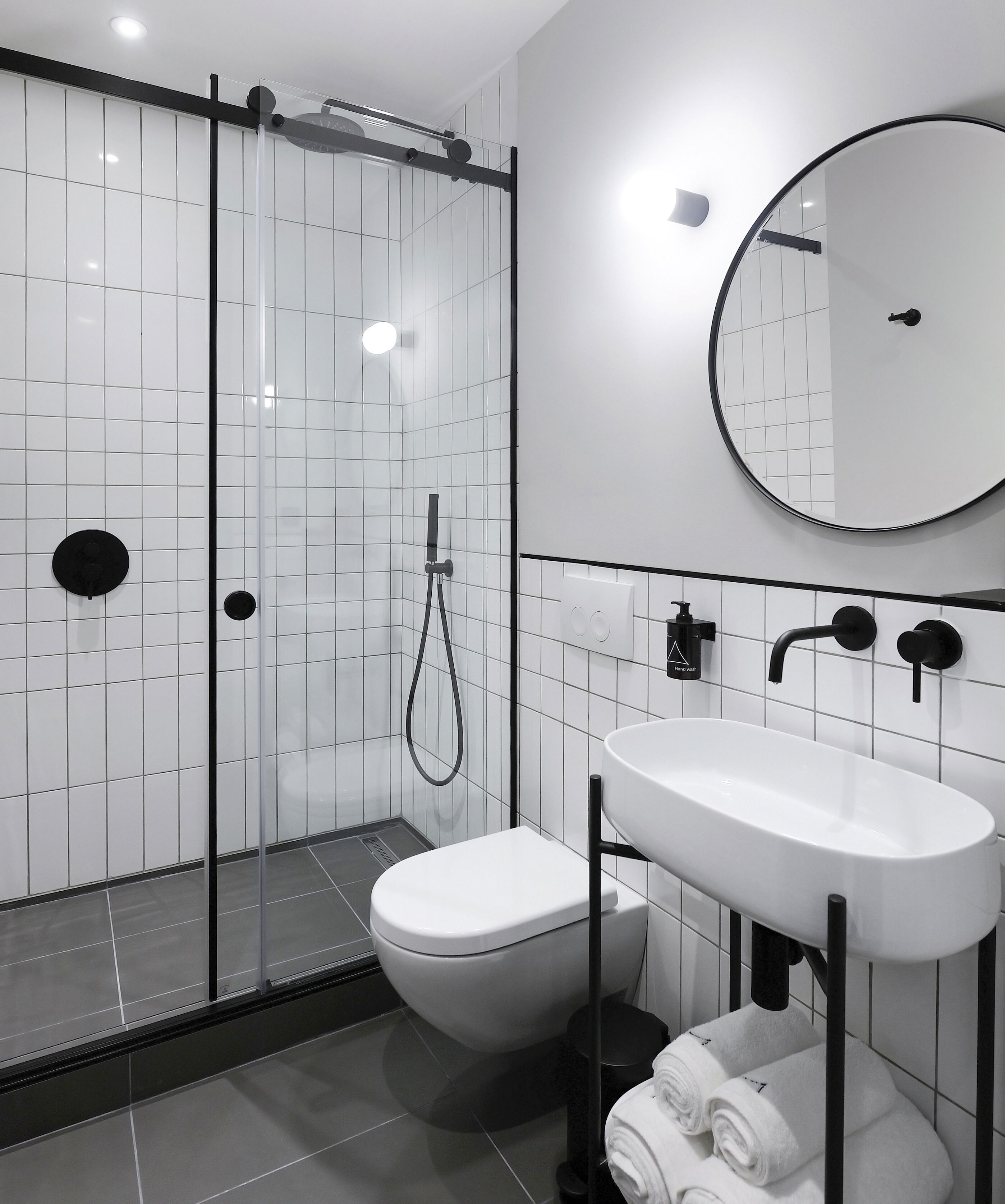 A modern bathroom with a glass-enclosed shower, a white toilet, a sink with a mirror, and neatly rolled towels.