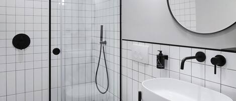 A modern bathroom with a glass-enclosed shower, a white toilet, a sink with a mirror, and neatly rolled towels.