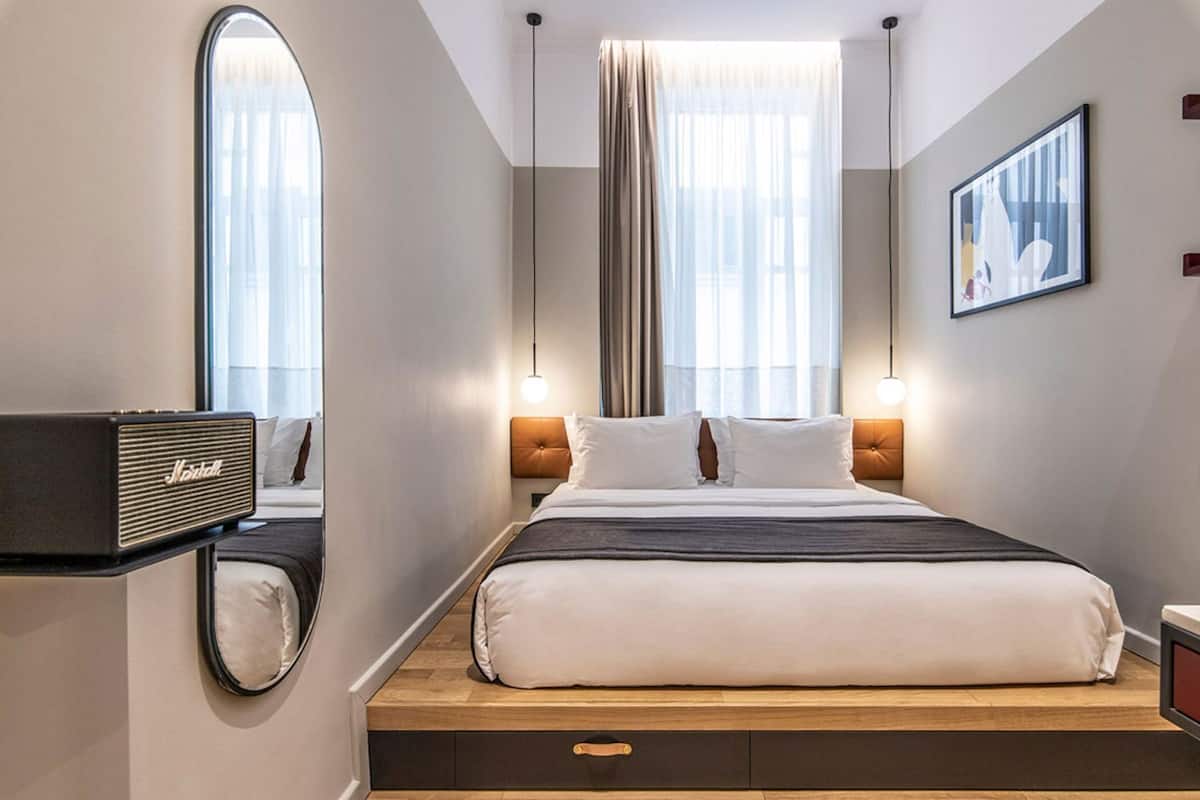 Une chambre d’hôtel avec un lit, un grand miroir, un haut-parleur Marshall et un tableau encadré au mur.
