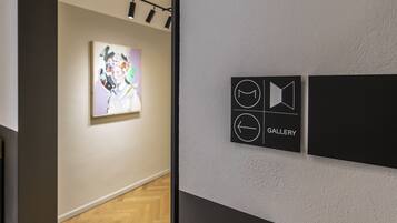 An art gallery with a modern interior, featuring a wooden floor and a wall-mounted sign indicating the gallery's direction.