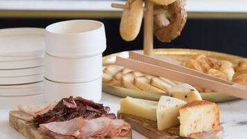 A breakfast buffet with various cheeses, meats, and pastries.