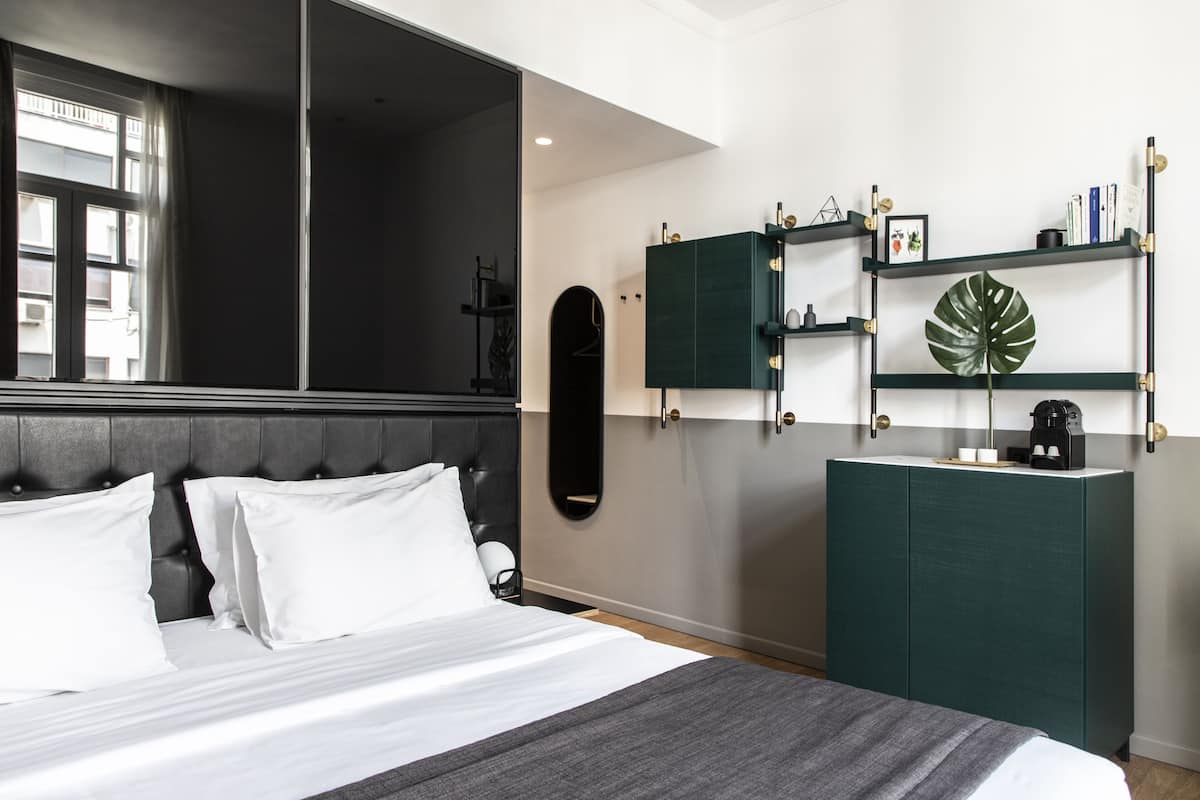 Ein modernes Schlafzimmer mit einem Bett, einer dunkelbraunen Kopfteil, einem grünen Schrank und einer großen Pflanze auf einem Regal.