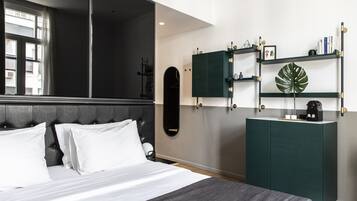 Un dormitorio moderno con cama, cabecera oscura, un mueble verde y una planta grande en una estantería.