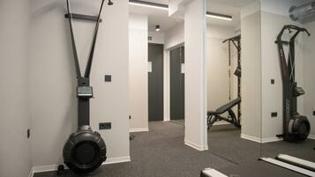 Un gimnasio con equipo de ejercicio, cinta de correr y pared con espejos.
