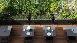 Un espace de restauration en plein air avec des tables pour deux, entouré d’un sol en bois et de verdure.