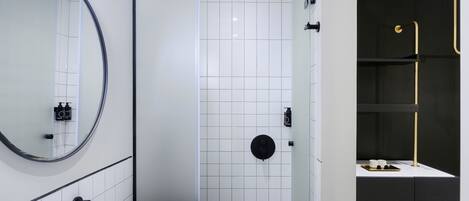 A modern bathroom with a white sink, a round mirror, a shower with a black control panel, and a dark-toned vanity area.