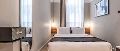 A modern hotel room with a large bed, a bedside table with a radio, a mirror, and a framed picture on the wall.