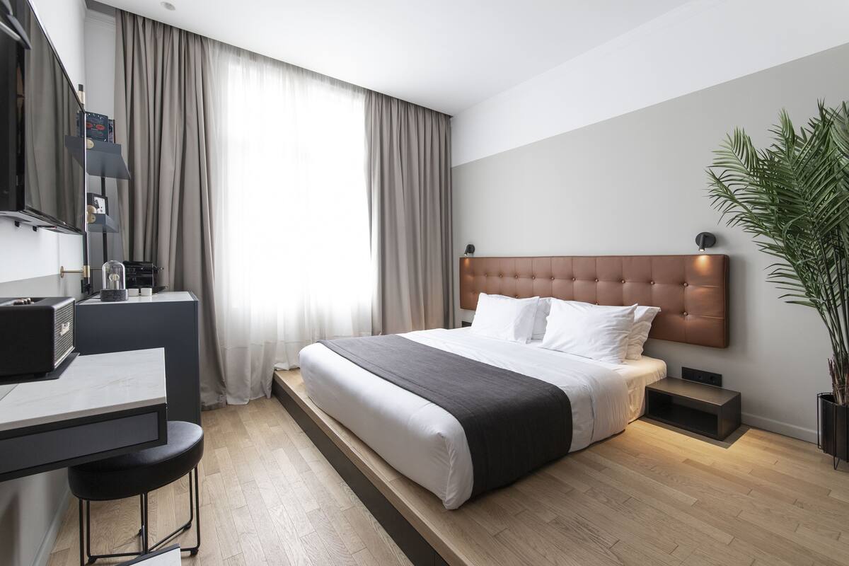 Une chambre d’hôtel moderne, équipée d’un lit, d’un bureau et d’une grande fenêtre avec des rideaux.
