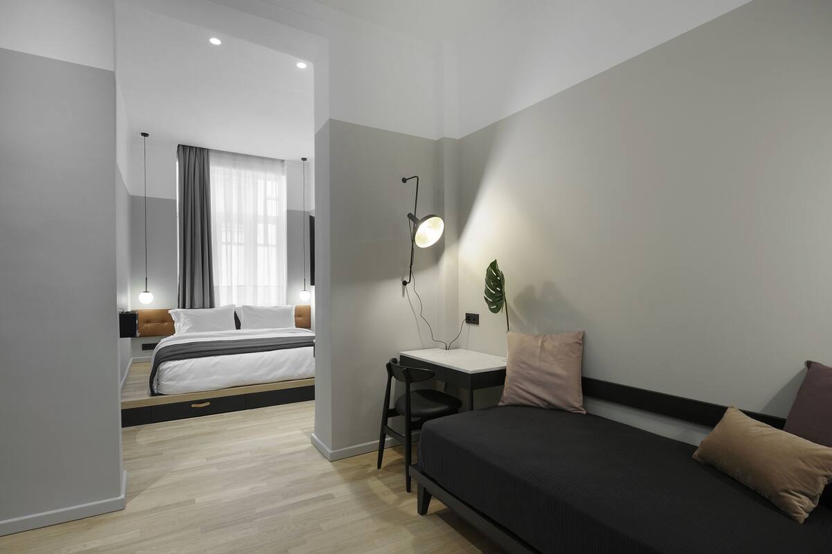 Ein modernes Hotelzimmer mit Bett, Schreibtisch und Stuhl. Auf dem Schreibtisch steht eine Lampe und an der Wand ein Zimmerpflanze.