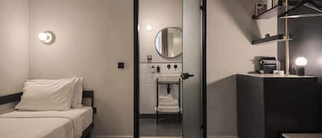 Una habitación de hotel moderna con cama, baño con lavamanos y espejo, y zona de escritorio.