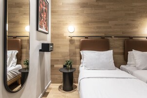 Habitación de hotel con dos camas, un espejo redondo, una mesita con una planta y una lámpara de pared.