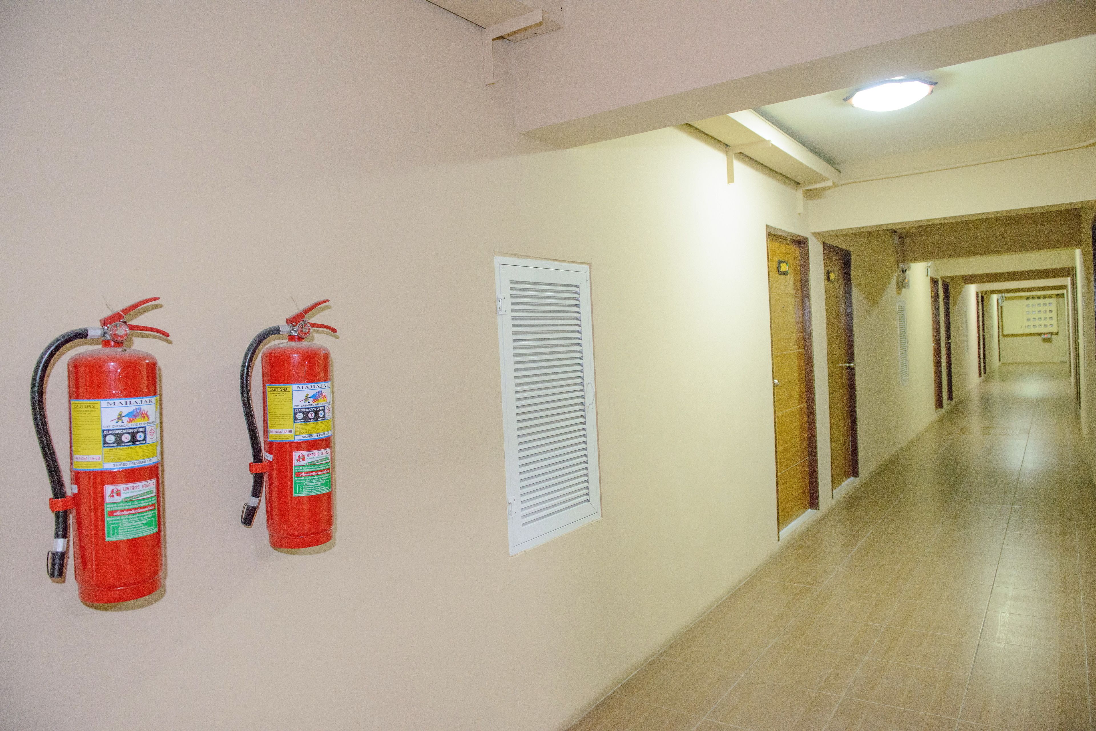 A hallway with two fire extinguishers mounted on the wall and a window with blinds.