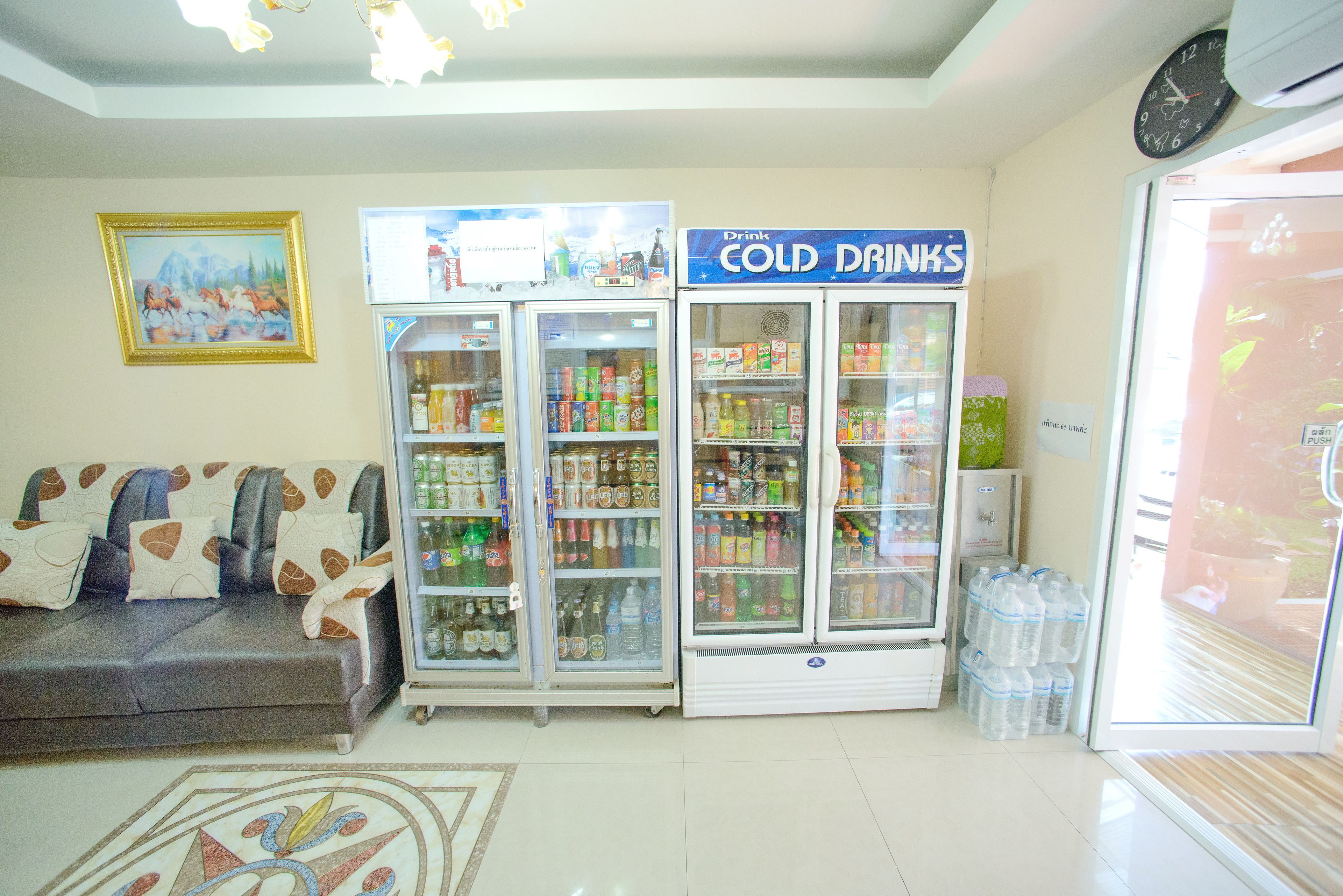 Habitación con sofá, dos refrigeradores llenos de bebidas, un reloj y un cuadro en la pared.