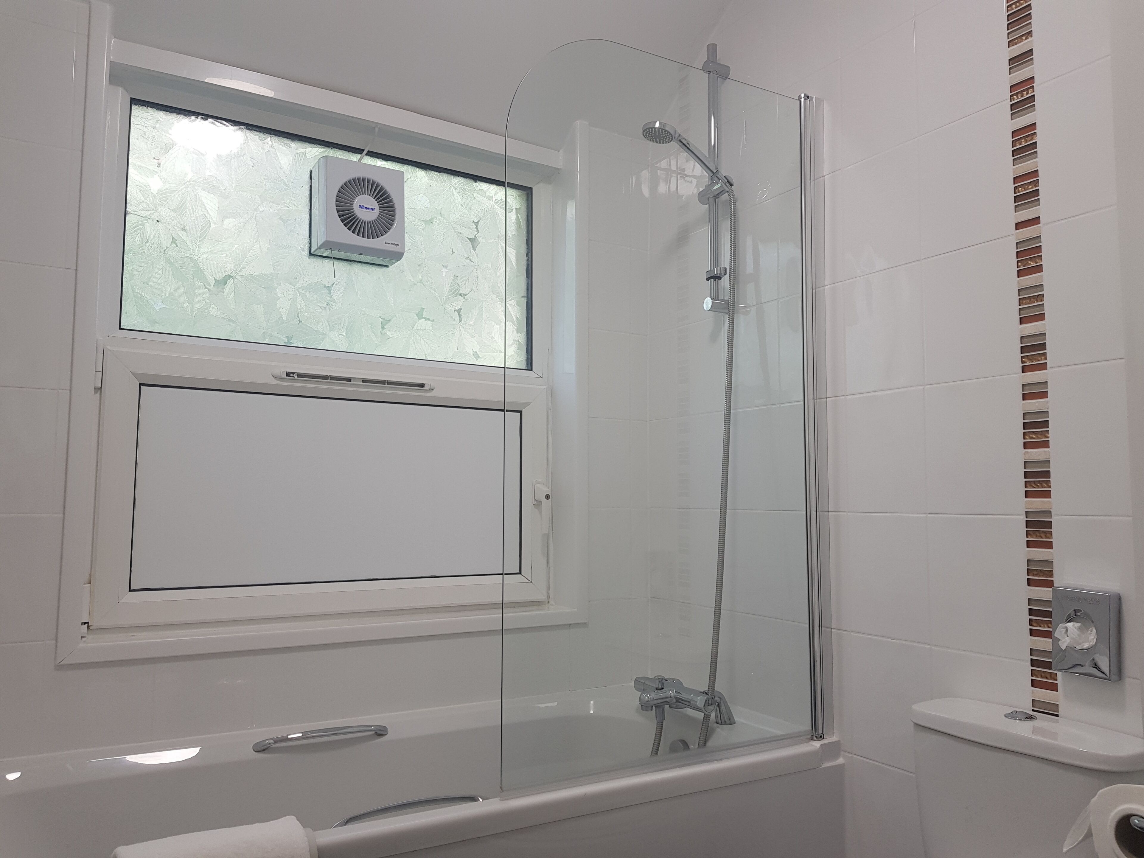 Een moderne badkamer met een douche met glazen wand, een raam met geëtste glas en een toilet met wasbakje.
