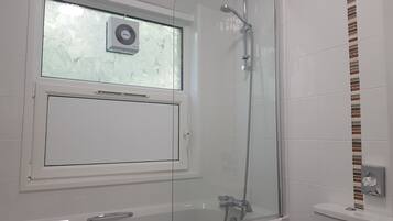 Een moderne badkamer met een douche met glazen wand, een raam met geëtste glas en een toilet met wasbakje.
