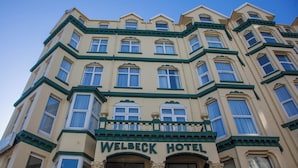 Een meerlaags hotel met een klassieke architectuur, met een opvallende ingang en een balkon, waarop de naam "WELBECK HOTEL" staat.