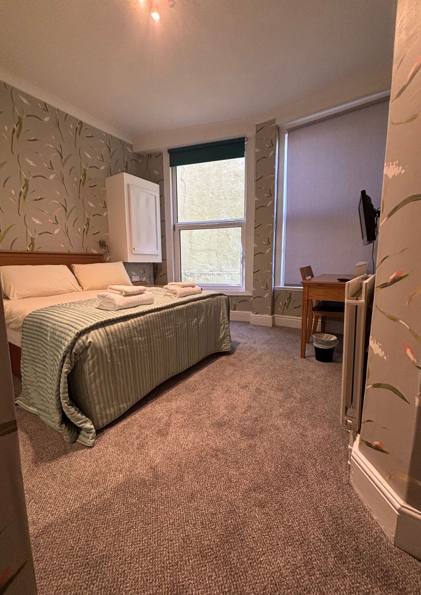A bedroom with a bed, a desk, a chair, and a window.