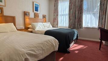 A hotel room with two beds, a red carpet, a wooden headboard, a desk, and a chair.