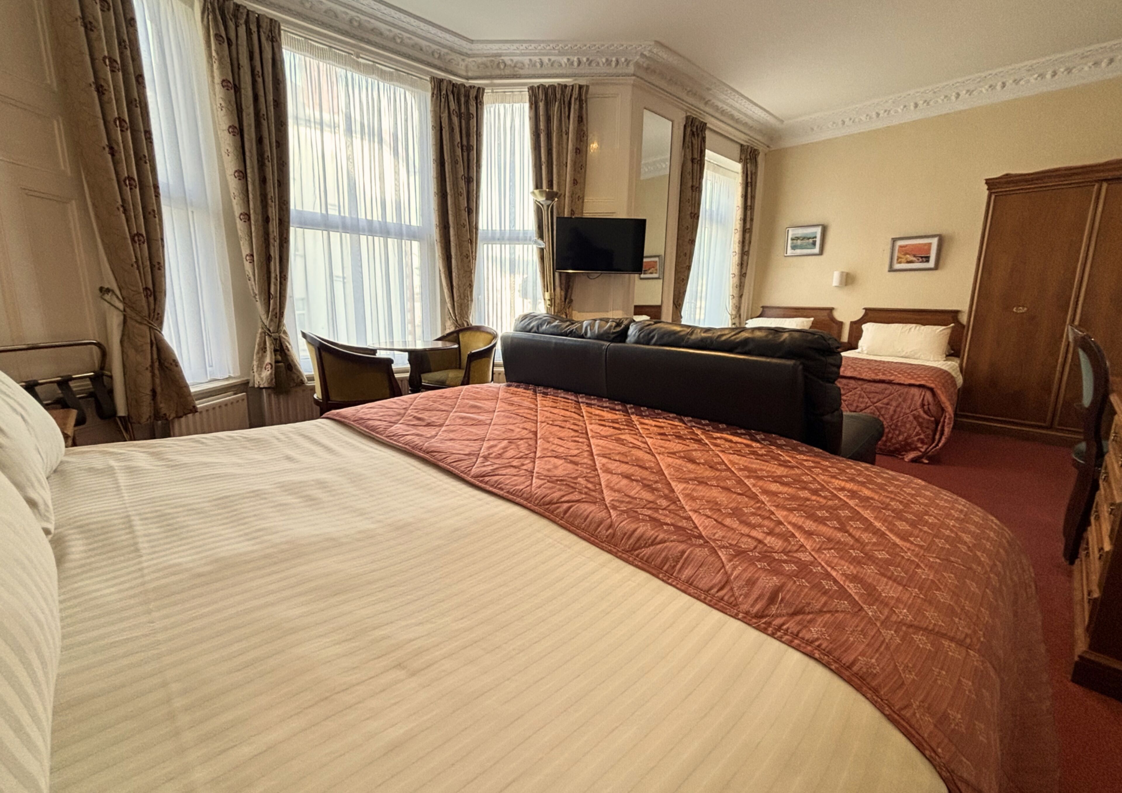 A hotel room with a large bed, a sofa, a desk, a television, and a wardrobe.